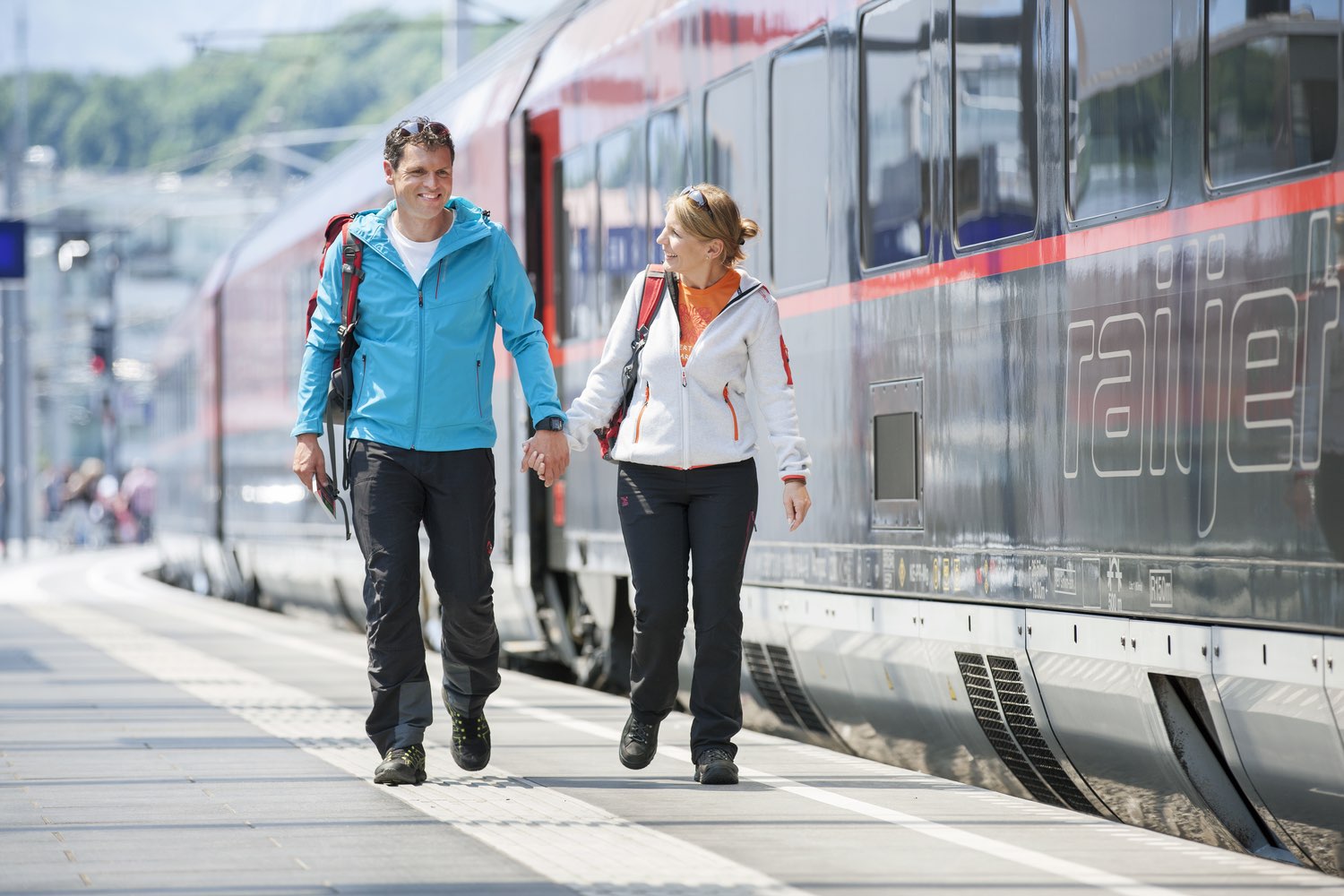 A couple walks along a train station platform with an Austrian Railjet train alongside
