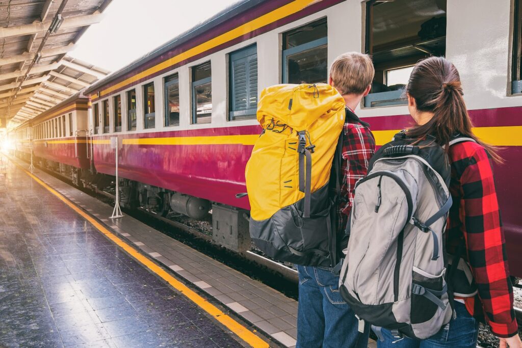 A couple board a train whilst wearing backpacks