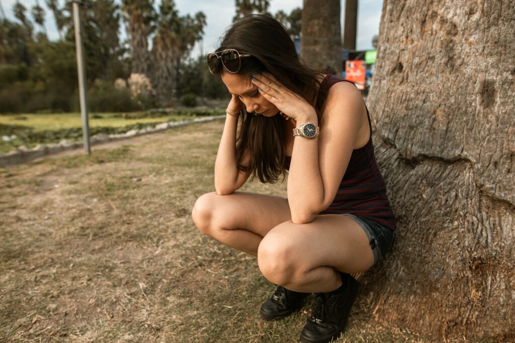 A woman crouches by a tree whilst looking stressed
